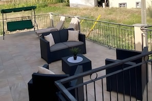 Uma área de estar externa com um sofá, uma mesa pequena e um toldo verde.