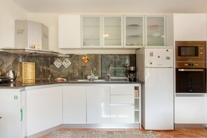A modern kitchen with white cabinets, a stainless steel range hood, a built-in oven, and a refrigerator.