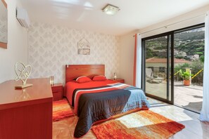 A bedroom with a bed, a nightstand, a dresser, a window with a view, and a wall with a decorative item.