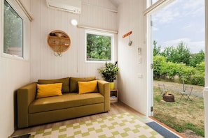 A room with a sofa, a potted plant, and a view of the outdoors.