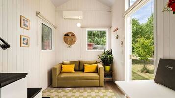 A cozy room with a sofa, a small table, a potted plant, and a view of greenery outside.