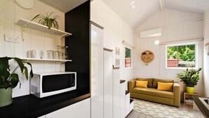 A modern kitchen with white cabinetry, a microwave, a black countertop, a yellow sofa, and a window with a view of greenery. - The Perch in Korweinguboora, Victoria (Korweinguboora)