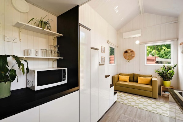 A modern kitchen with white cabinetry, a microwave, a black countertop, a yellow sofa, and a window with a view of greenery.