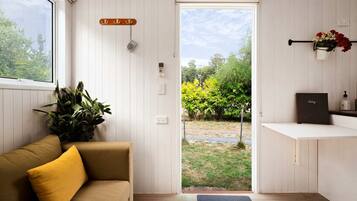 A room with a sofa, a potted plant, a door leading outside, and a small shelf with a book and a bottle.