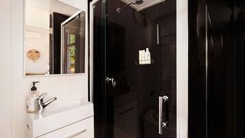 A modern bathroom with a white vanity, a glass shower enclosure, and a mirror with a wooden-framed inset.
