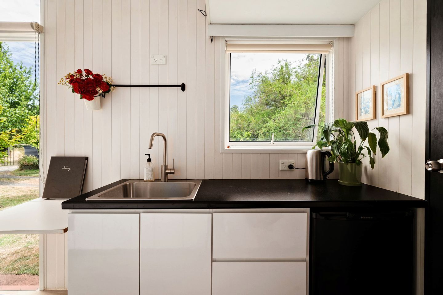 A modern kitchen with a black countertop, white cabinets, a stainless steel sink, and a window with a view of greenery.