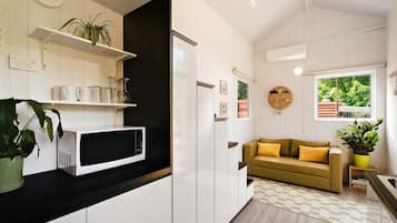 A modern kitchen with white cabinetry, a microwave, a black countertop, a yellow sofa, and a window with a view of greenery.
