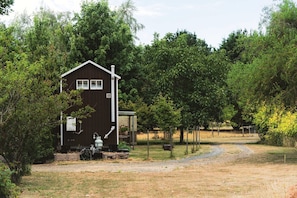A small, dark wooden cabin with a metal water tank and a small shed nearby.