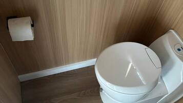 Un baño moderno y compacto con un inodoro, un pequeño bote de basura y un rollo de papel higiénico en la pared.