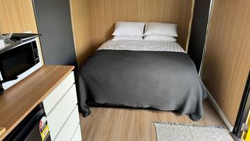Una habitación pequeña con una cama, un escritorio con microondas y un armario.