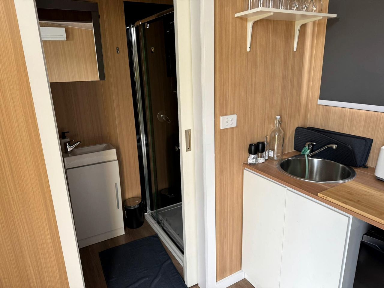 Una kitchenette compacta con un lavamanos, un refrigerador pequeño y un box de ducha de vidrio.
