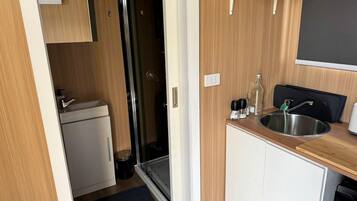 Una kitchenette compacta con un lavamanos, un refrigerador pequeño y un box de ducha de vidrio.