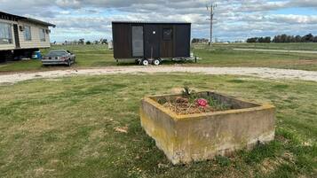 A mobile home with a trailer attached, a concrete planter with a flower, and a car parked nearby.