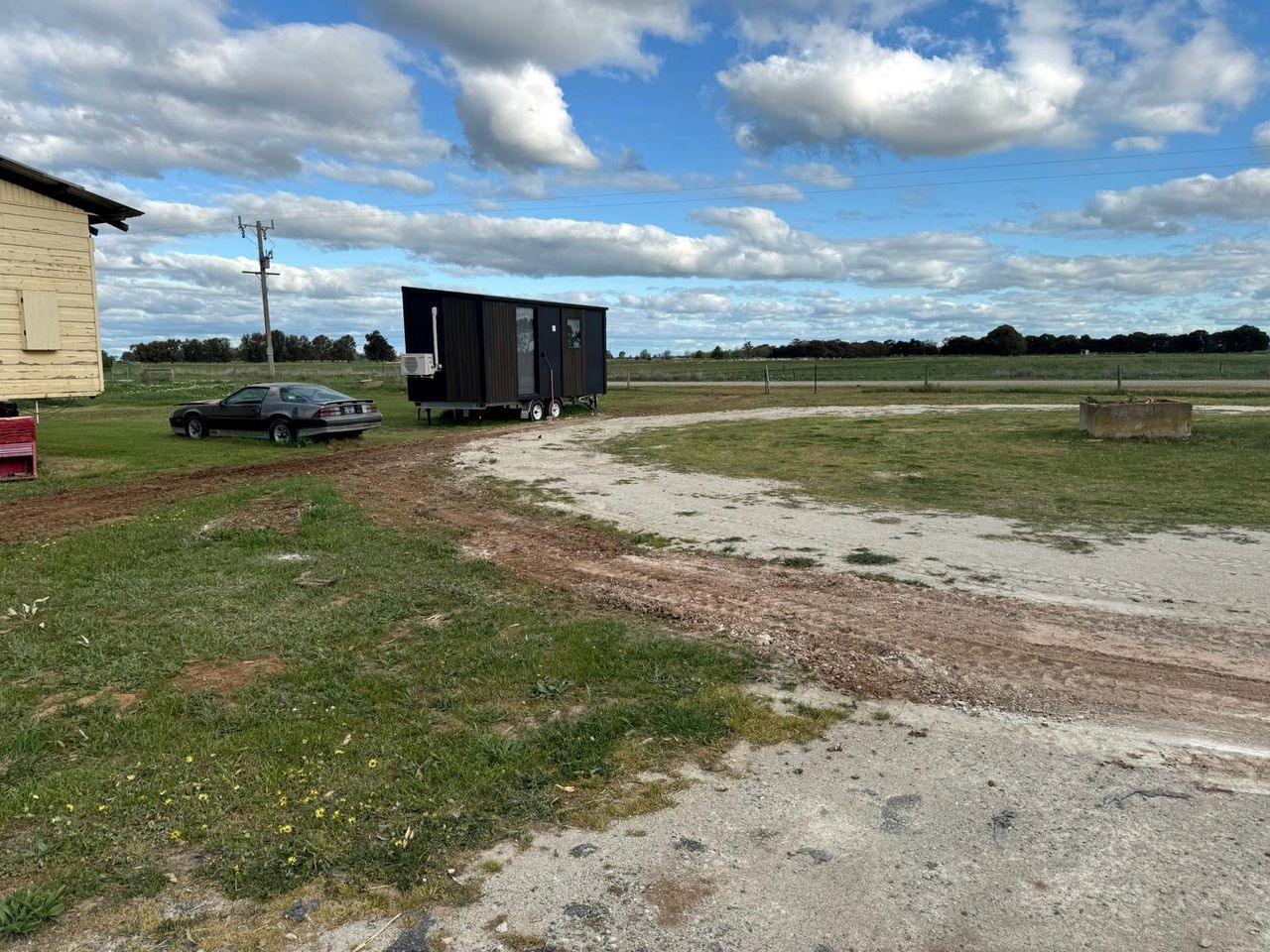 A rural setting with a trailer, a car, and a building.