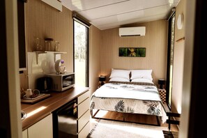 A compact bedroom with a bed, bedside tables, a microwave, and a window.