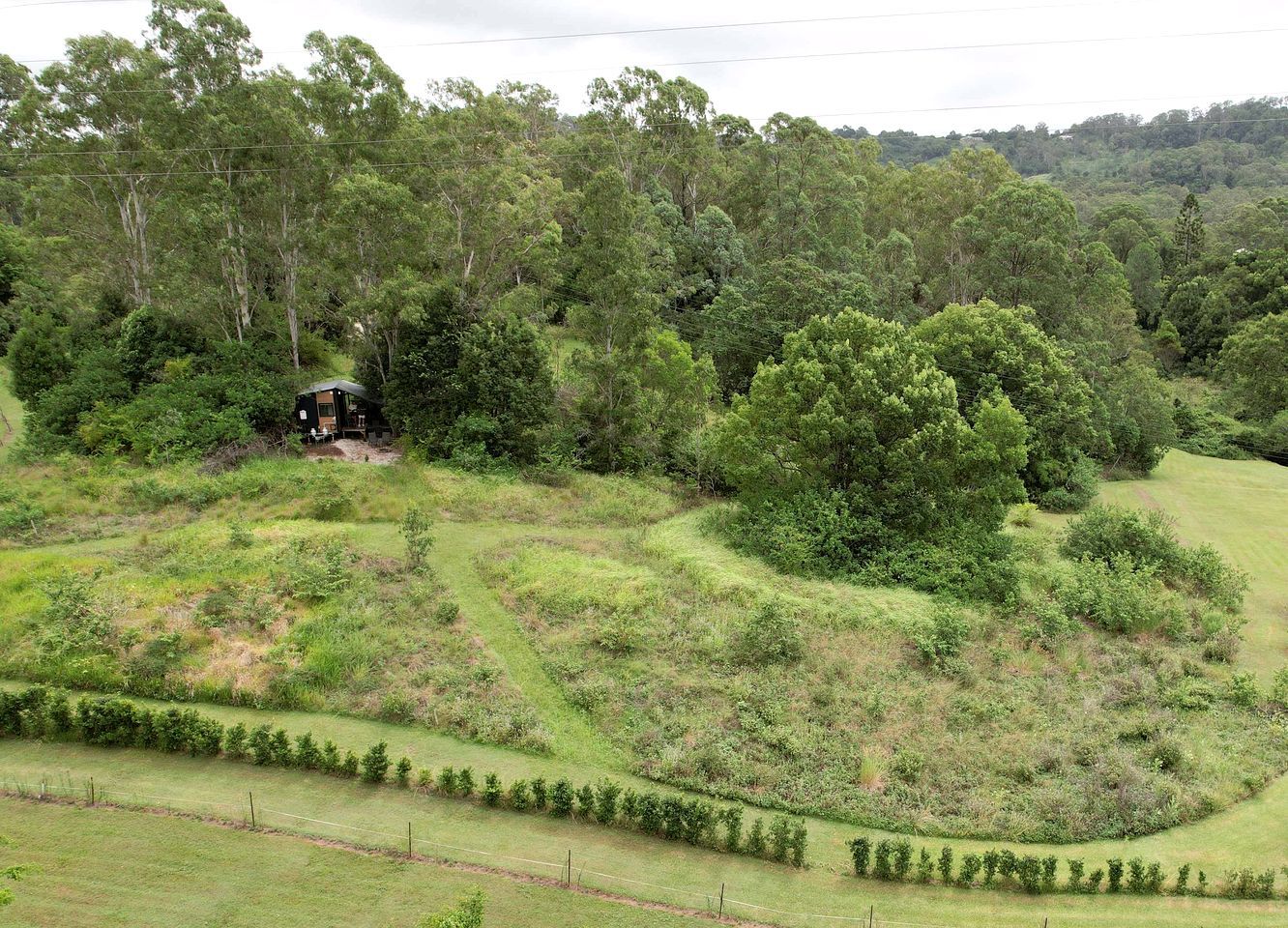 A rural landscape with a house surrounded by dense trees and rolling hills.