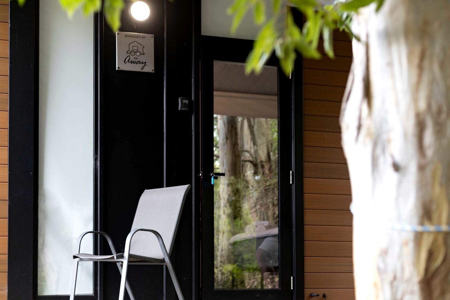 A chair outside a building with a 'Managed by' sign, a wooden wall, and a tree.