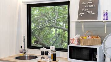 A kitchen with a sink, a microwave, and a window with a view of trees. There's a welcome sign above the window and a basket with snacks on the counter.