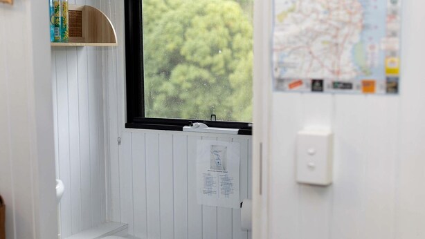 Un baño pequeño y blanco con inodoro, una ventana y un mapa en la pared.