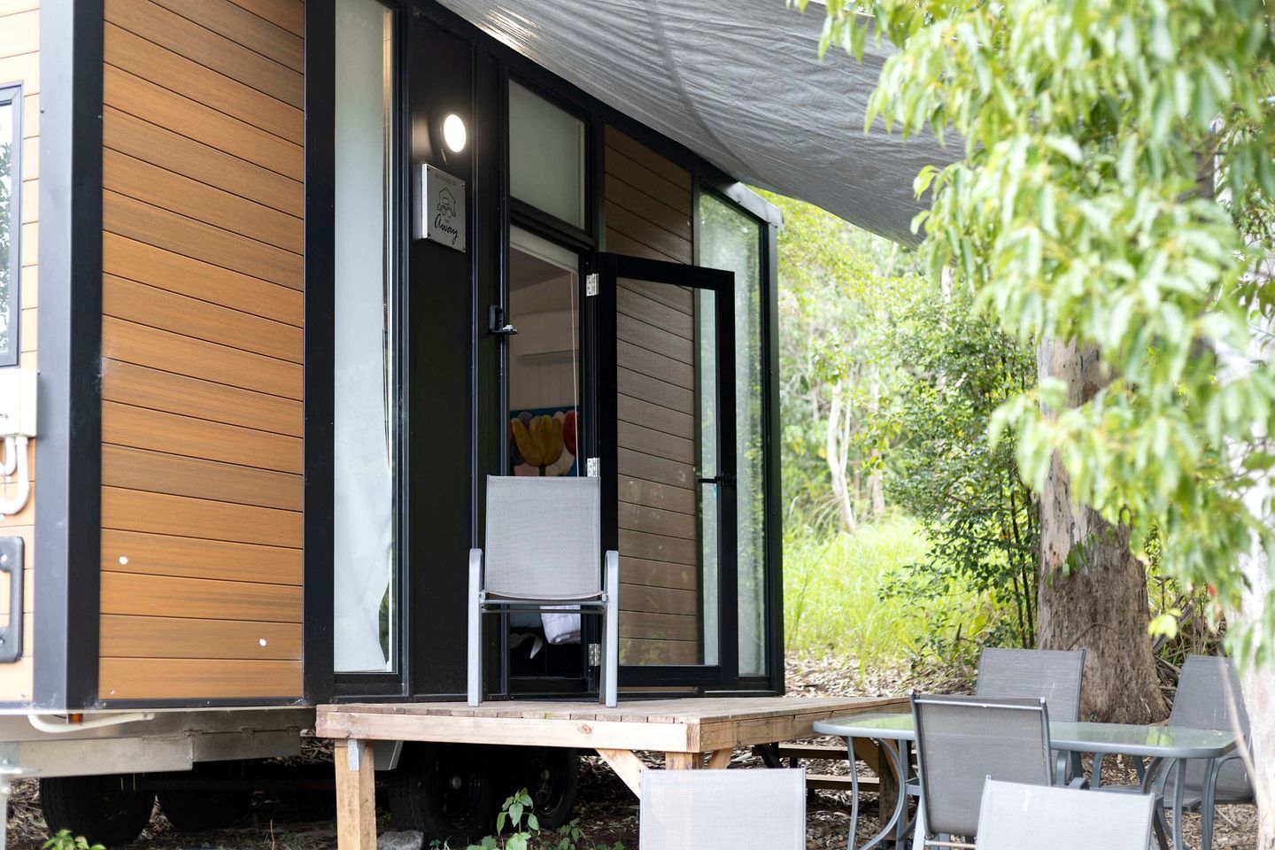Un bâtiment moderne avec une façade en bois, une porte-fenêtre coulissante et un petit espace extérieur aménagé avec des chaises et une table en métal.