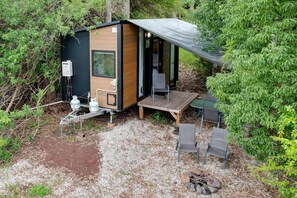 A compact, modern cabin with a wooden exterior, a small deck, and a fire pit.