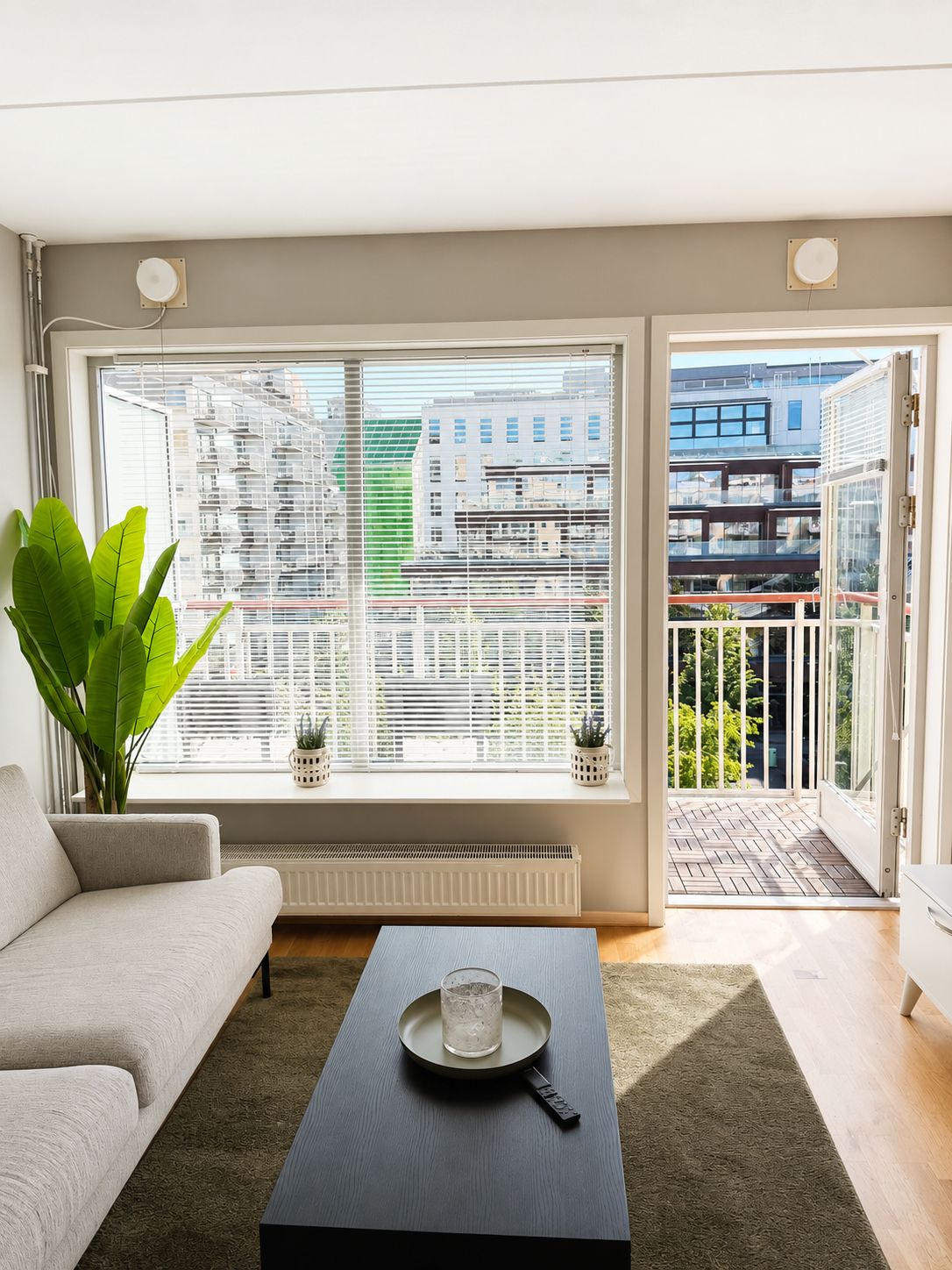 A modern living room with a sofa, a coffee table, and a view of a cityscape through large windows.