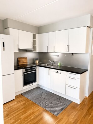 Eine moderne Küche mit weißen Schränken, einer schwarzen Arbeitsplatte, einem eingebauten Backofen und einer Spüle aus Edelstahl.