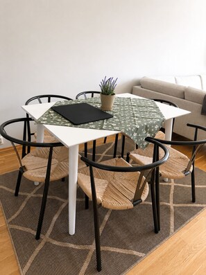 Ein Essbereich mit einem weißen Tisch, vier Stühlen, einer grünen Tischdecke und einem Blumentopf.