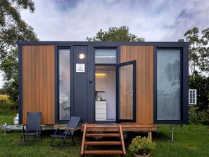A modern, compact cabin with a wooden exterior, a visible kitchen area, and a deck with seating. - Picturesque Secluded Tiny House in Bullahdelah, New South Wales (Bulahdelah)