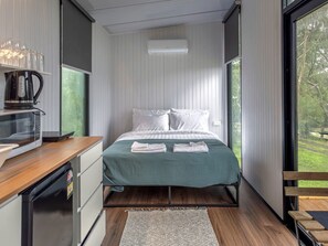 A modern bedroom with a bed, a coffee maker, a microwave, and a view of the outdoors.
