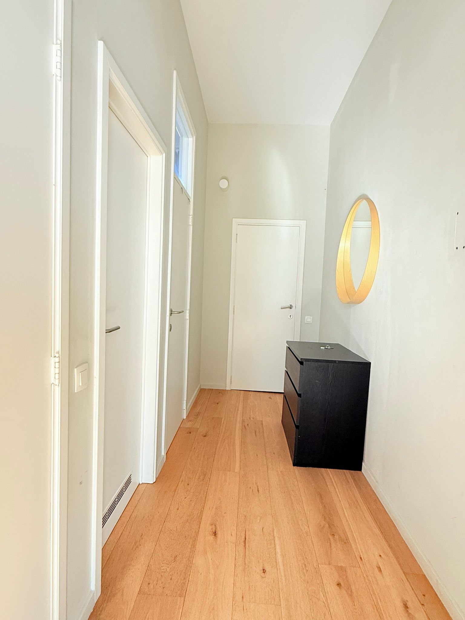 Un pasillo con suelo de madera, paredes blancas y un mueble negro para almacenamiento.