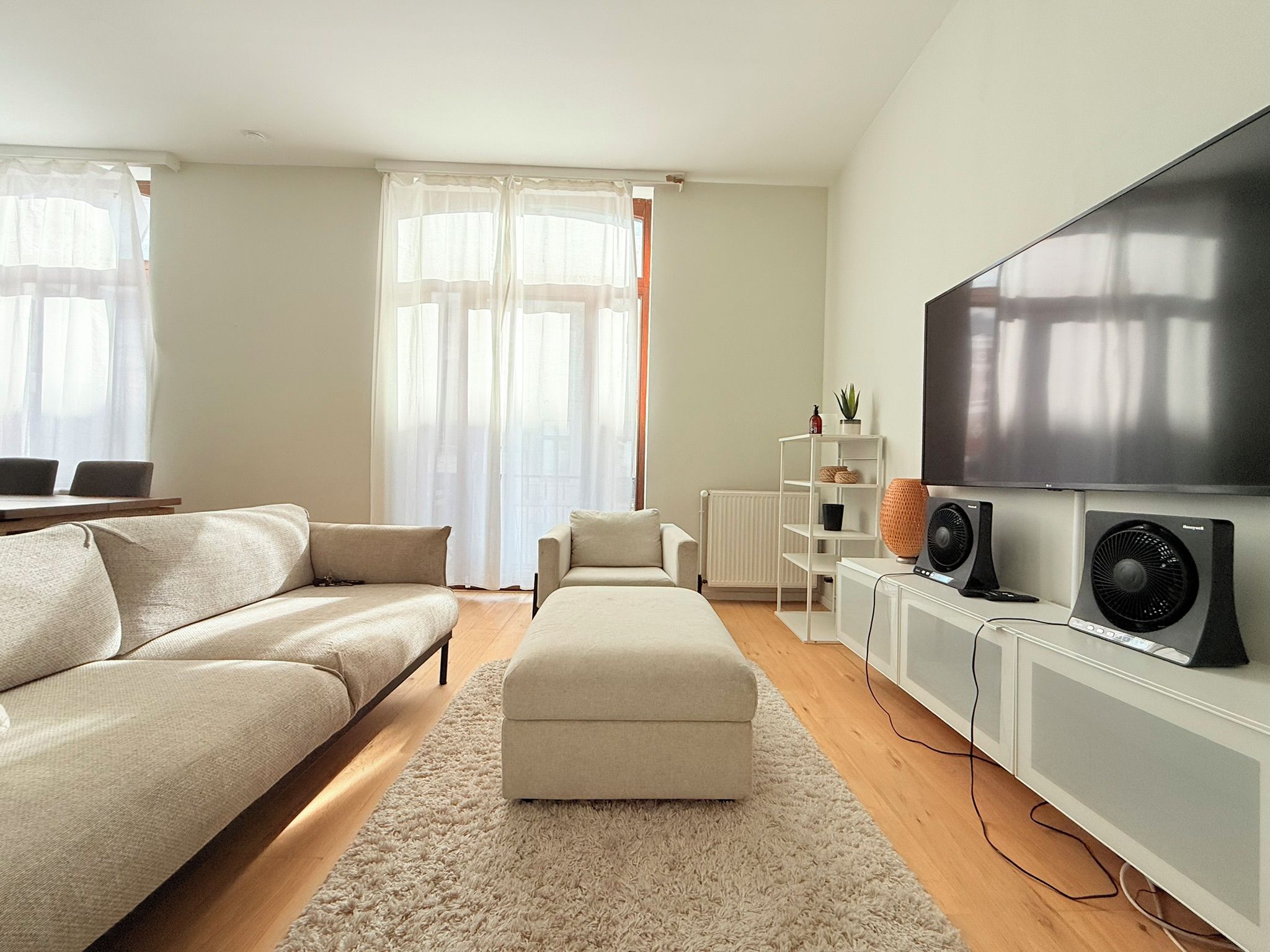 A modern living room with a sofa, ottoman, TV, speakers, and a radiator.