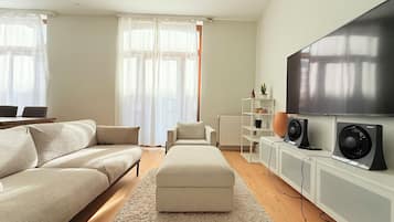 A modern living room with a sofa, ottoman, TV, speakers, and a radiator.