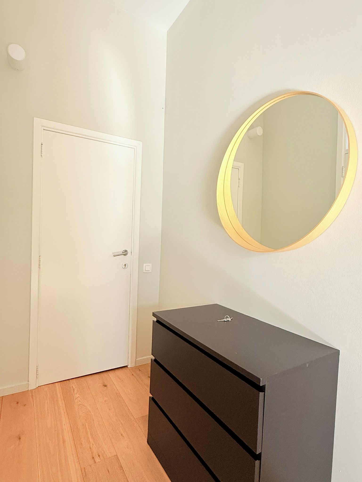 Una habitación con una puerta blanca, un aparador negro y un espejo redondo en la pared.