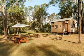 A wooden cabin with a metal roof, surrounded by trees, and equipped with a picnic table and chairs.