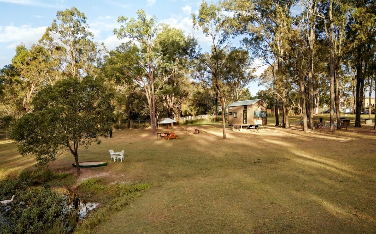 A grassy outdoor area with a small cabin, picnic tables, and a white chair.