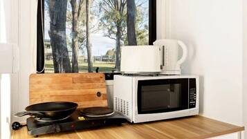 Uma cozinha compacta equipada com micro-ondas, cafeteira e frigideira, sobre uma bancada de madeira.