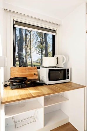 A compact kitchenette with a microwave, a coffee maker, and a frying pan on a wooden countertop.