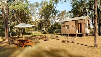 A wooden cabin with a metal roof, surrounded by trees, and equipped with a picnic table and chairs.