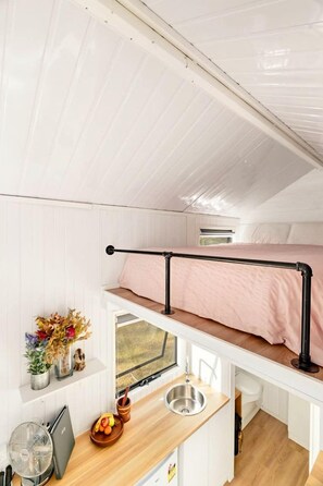 Quarto compacto e bem iluminado com beliche, pequeno espaço de cozinha e janela que traz luz natural.