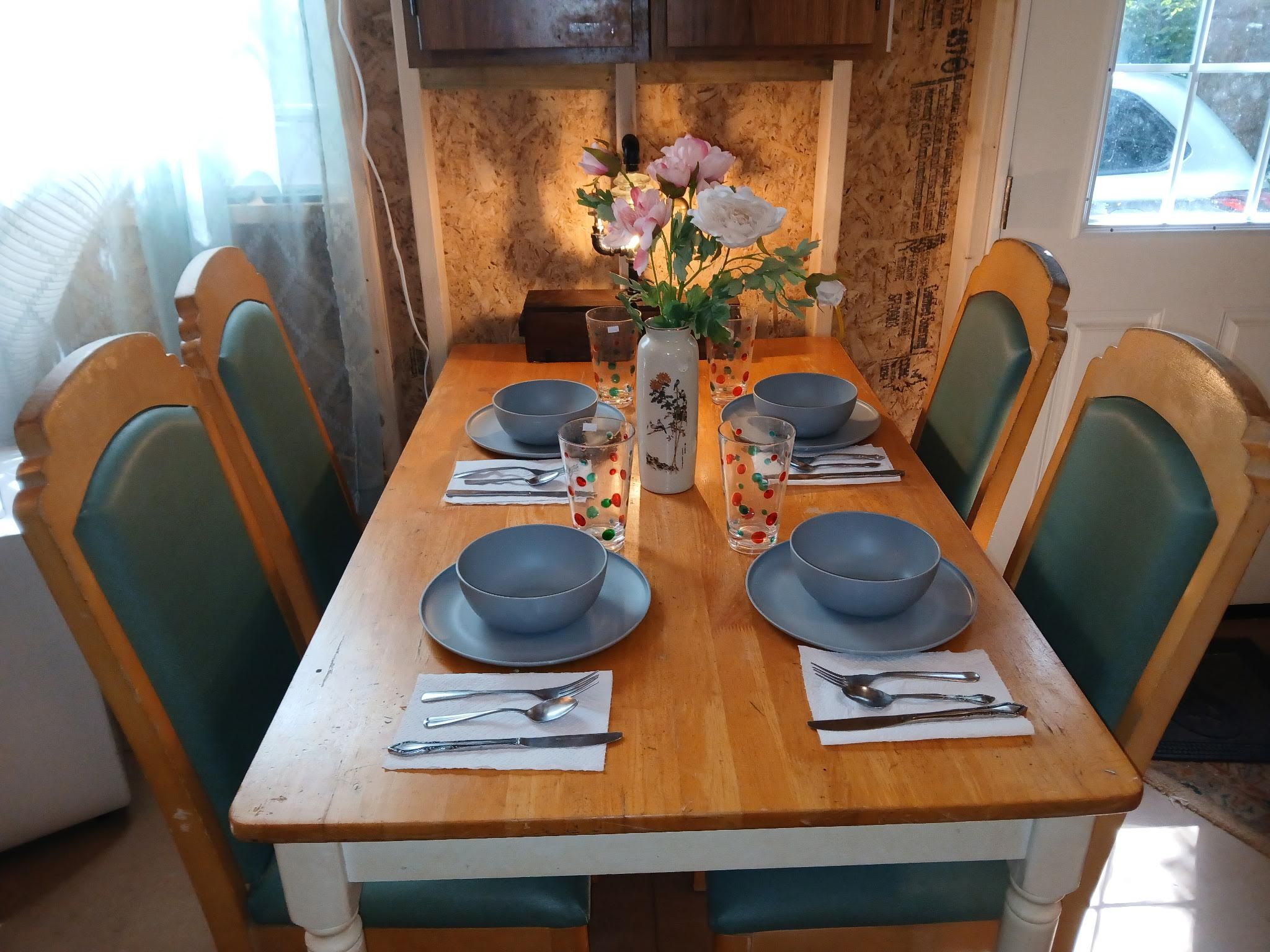 Una mesa de madera para comer con seis sillas, dispuesta para cuatro personas, con platos, tazones y cubiertos.