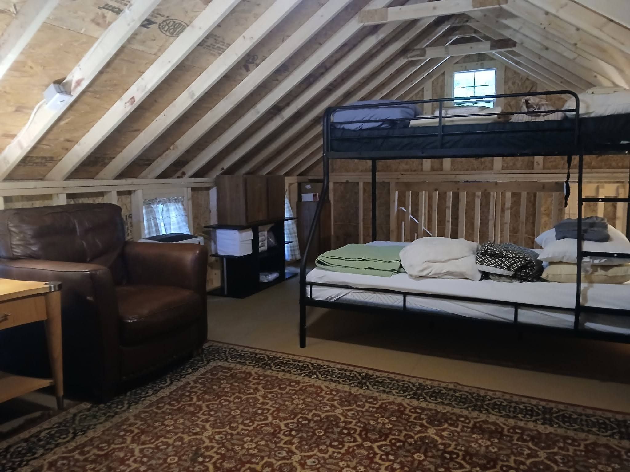 Ein gemütliches Dachzimmer mit Etagenbett, Ledersessel, kleinem Schreibtisch und einem gemusterten Teppich.