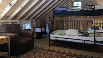 Ein gemütliches Dachzimmer mit Etagenbett, Ledersessel, kleinem Schreibtisch und einem gemusterten Teppich.