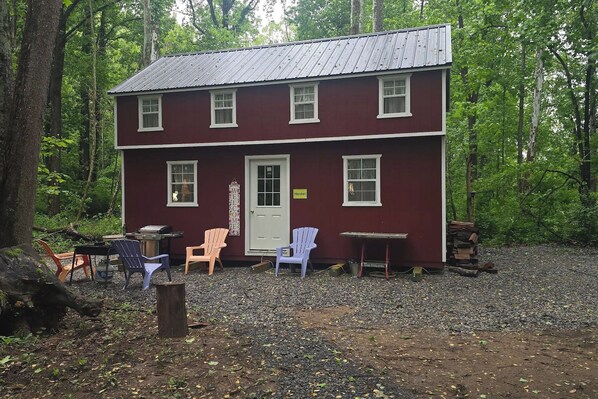 A two-story cabin with a red exterior, a front door, and a small porch area with outdoor seating.