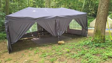 A tent set up in a forested area with a bench inside.