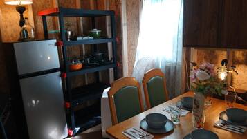 Ett kompakt kök med kylskåp, en hyllsektion och ett matbord med plats för två personer.