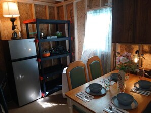 A compact kitchen with a refrigerator, a shelf unit, and a dining table set for two.