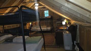 A dormitory-style room with bunk beds, a desk, a chair, and a radiator.