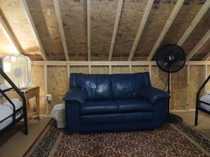 A room with a blue leather sofa, a standing fan, a patterned rug, and a small table with a lamp.