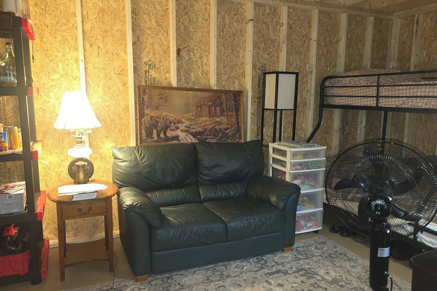 A room with a leather sofa, a lamp, a painting, a fan, and storage units.